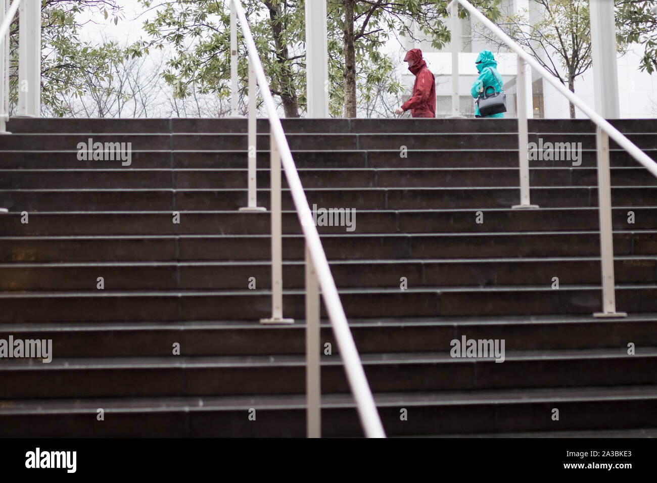 Mojar las escaleras conducen a una salida de lluvias como dos personas andando por en impermeables. Foto de stock