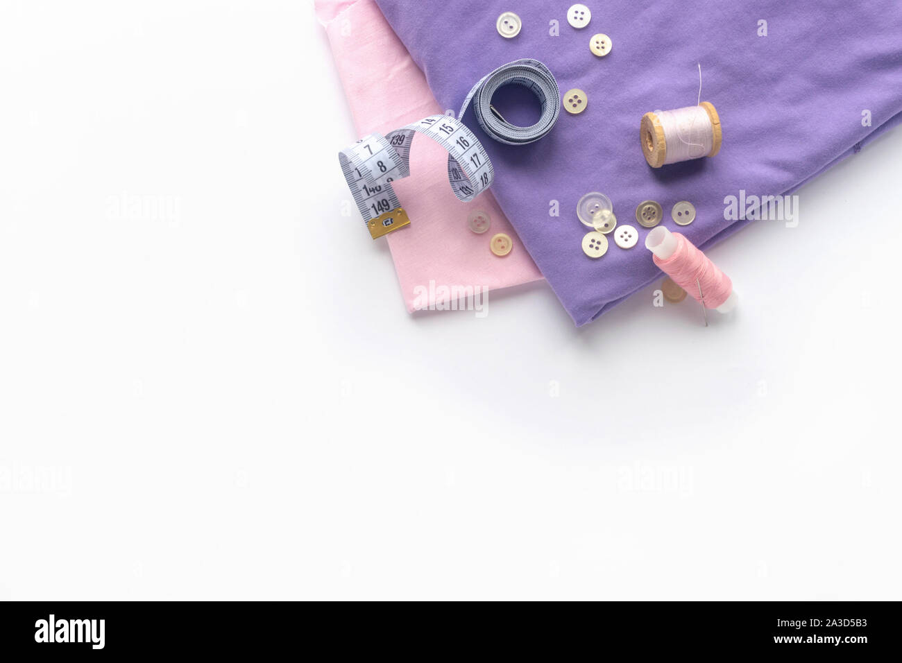 Accesorios de costura y tejido sobre un fondo blanco. Tela, hilos de costura, agujas de coser botones y centímetro. top view, flatlay Foto de stock