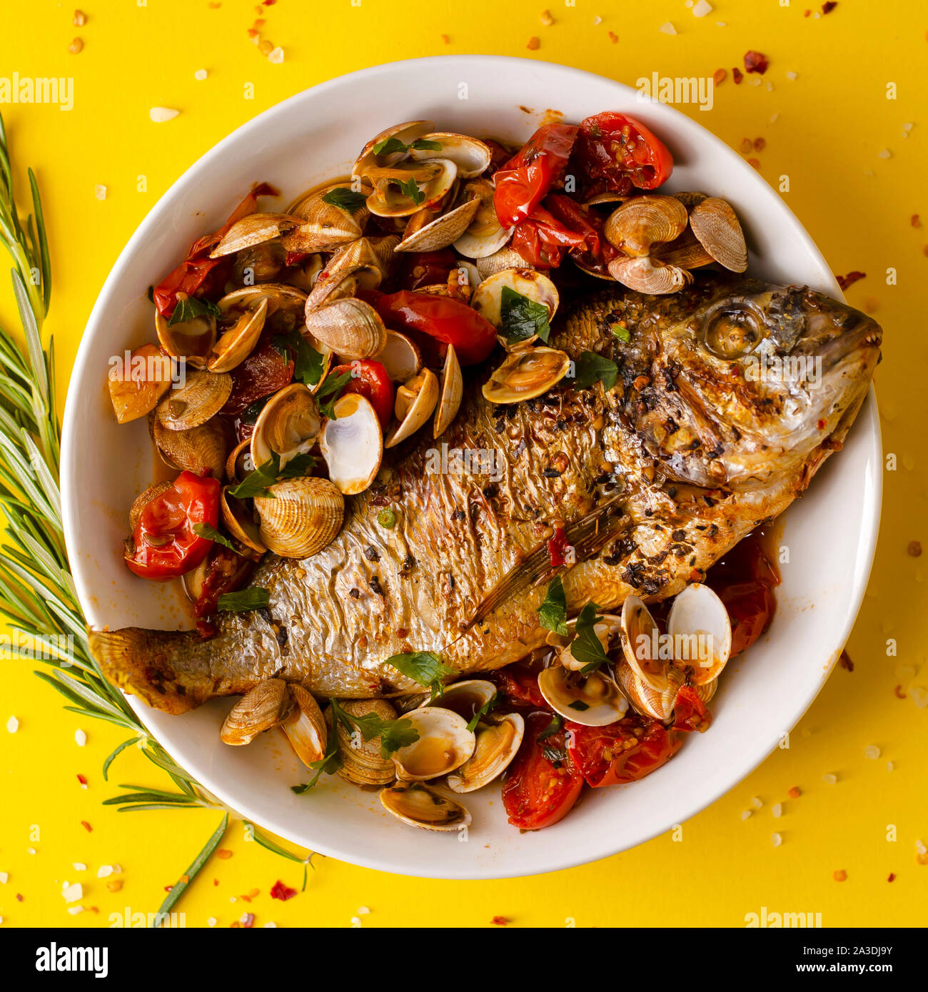 Dorada pescado a la parrilla con almejas en un cuenco blanco sobre fondo amarillo. Concepto de mariscos. Sobrecarga shotspace para texto Foto de stock