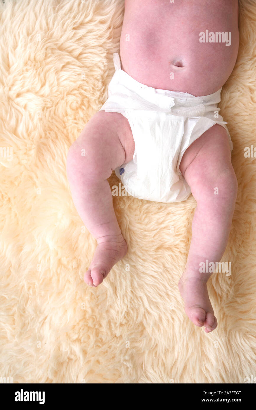 Las piernas del bebé recién nacido con pañales blancos pañales, sobre un fondo de pieles. Foto de stock