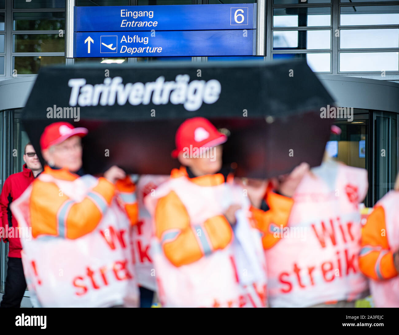 08 de octubre de 2019, Renania del Norte-Westfalia, Greven: Los empleados de las empresas de limpieza están vistiendo chalecos de huelga y un ataúd con la inscripción: "Convenios Colectivos" en el aeropuerto de Münster Osnabrück. Los limpiadores inició una huelga de advertencia de 24 horas el martes con el cambio temprano a las 6:00 a.m., esta fue la reacción de la Unión a las estancadas negociaciones sobre un marco acuerdo salarial para la limpieza comercial, un portavoz para el IB BAU dice. El tráfico aéreo se verá afectada porque no se permite a los aviones despegar sin limpieza. Se están realizando campañas paralelas en los aeropuertos de Francfort y Berlín-Tegel. Foto de stock