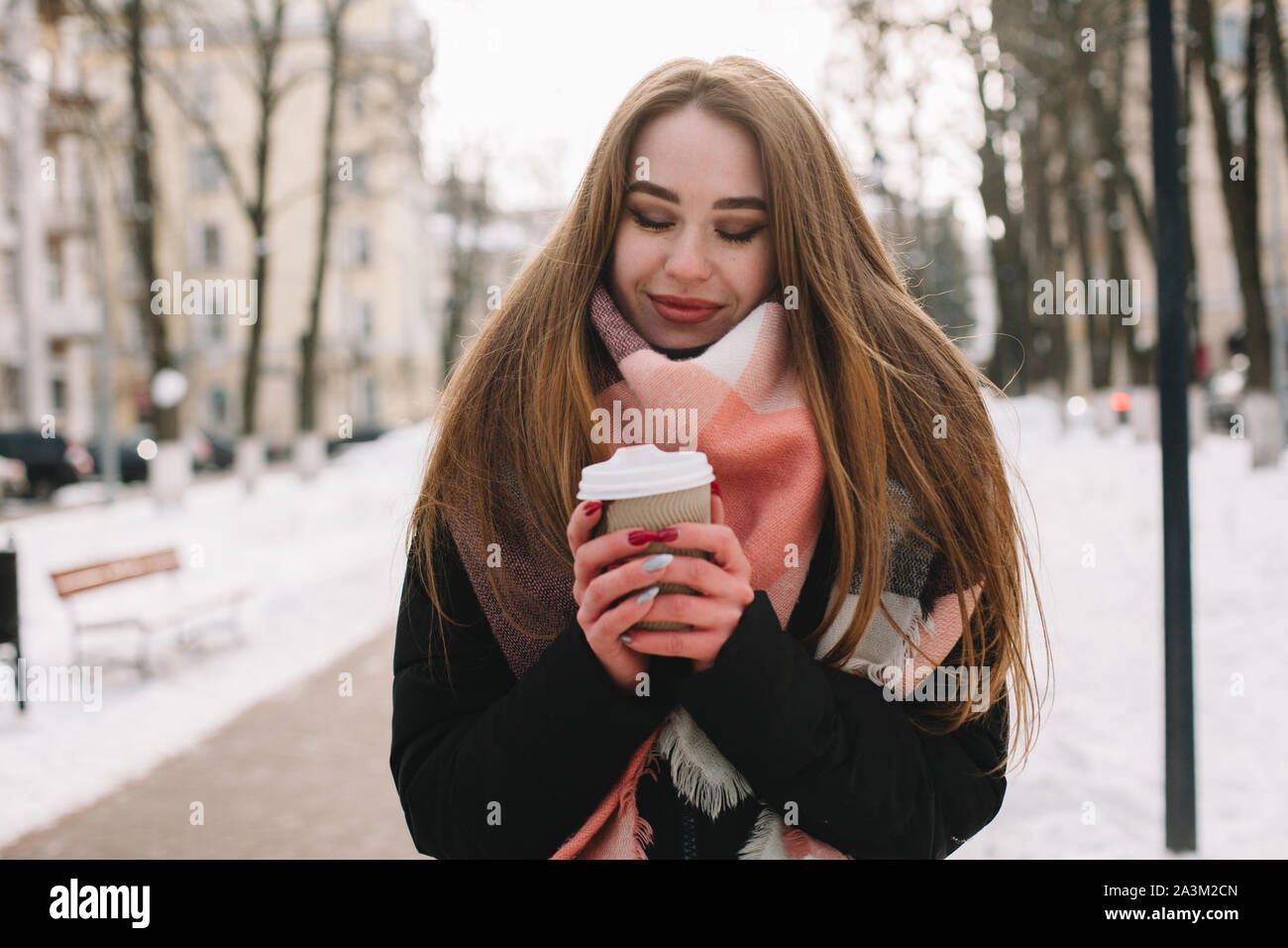 Feliz joven con copa desechable vistiendo ropa de abrigo mientras caminaba por las calles de la ciudad durante el invierno Foto de stock