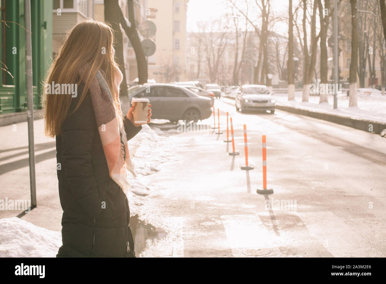 Mujer con vaso desechable en ropa de abrigo, cruzando las calles de la ciudad en invierno Foto de stock