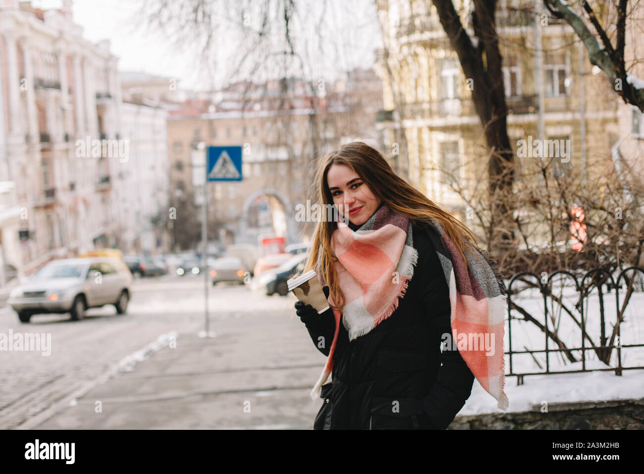 Feliz mujer con vaso desechable en ropa de abrigo, de pie en las calles de la ciudad durante el invierno Foto de stock