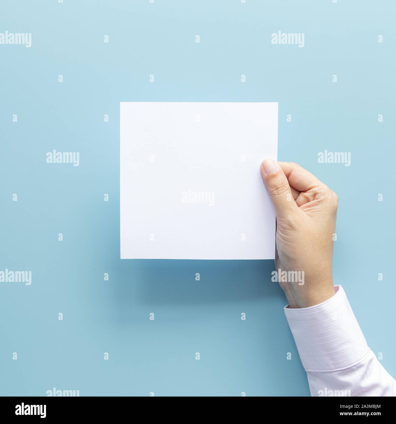 Mujer mano sujetando la hoja de papel en blanco sobre fondo azul aislado con espacio de copia. Foto de stock