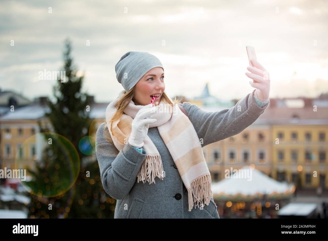 Mujer joven en el mercado de Navidad, comiendo y tomando selfie bastón de  caramelo. Chica en tejido cálido gorro y bufanda. Iluminado y decorado  justo quioscos, tiendas Fotografía de stock - Alamy