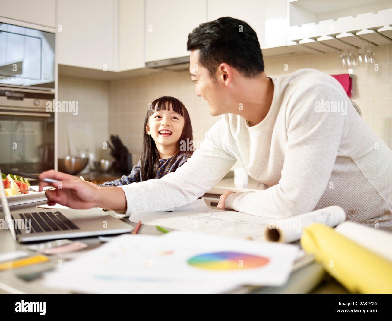 Hombre asiático joven diseñador free lance padre trabajando en casa teniendo cuidado de la hija. Foto de stock