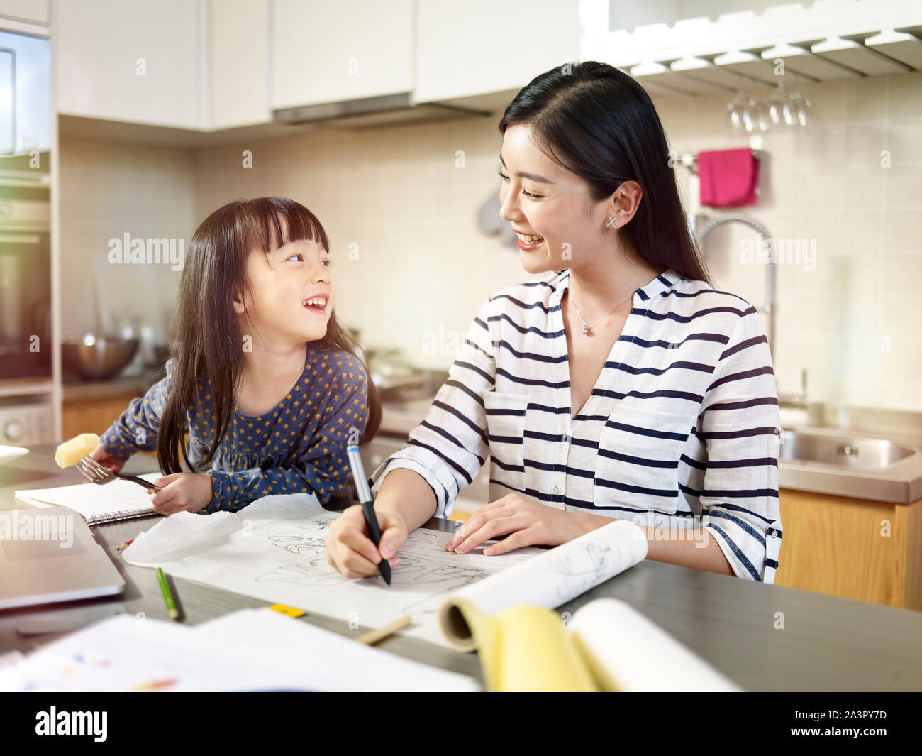Jóvenes profesionales de diseño asiático madre trabajando en casa teniendo cuidado de la hija. Foto de stock