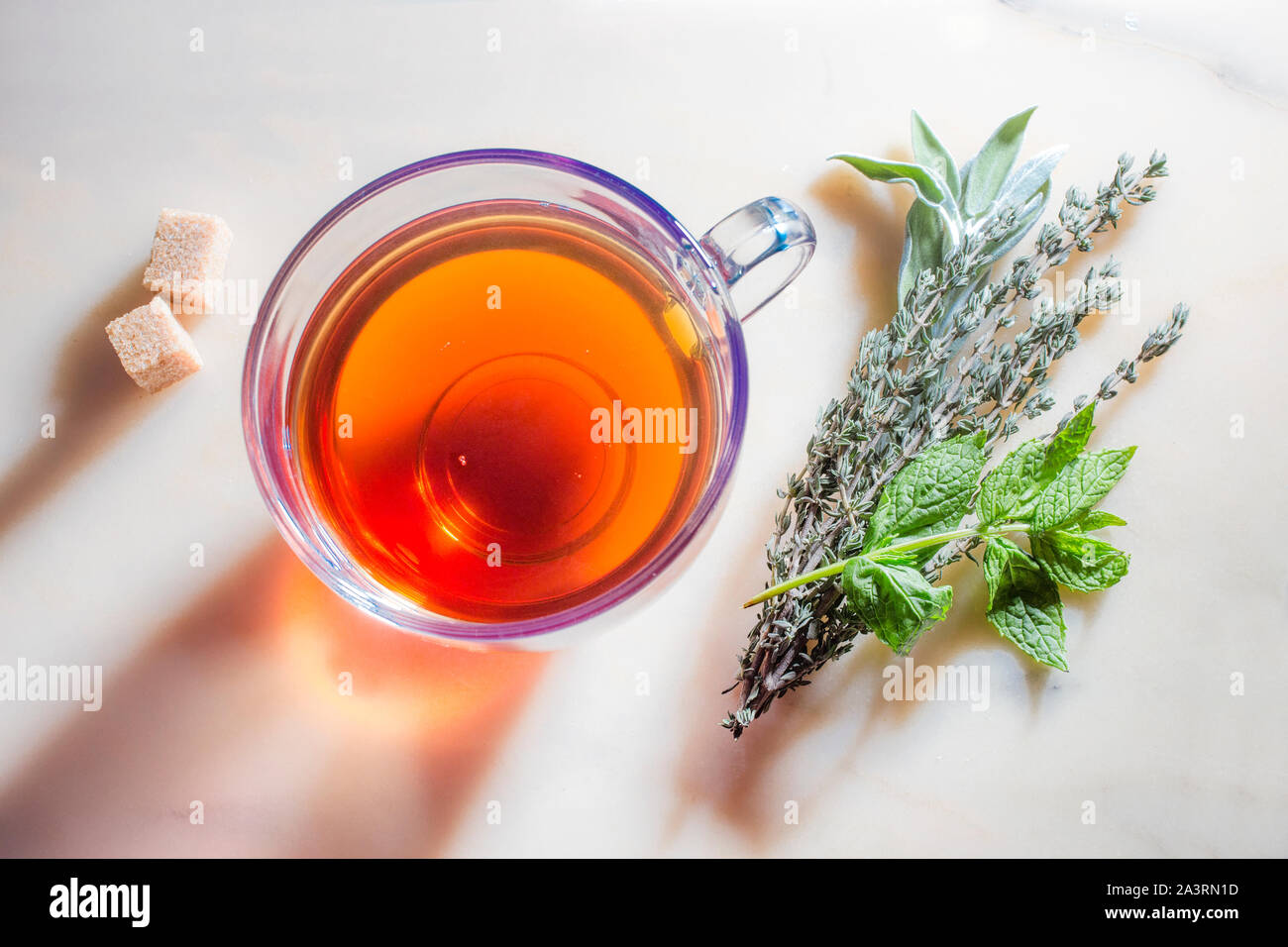 Imagen de un vaso con té, hierbas y azúcar en la superficie de mármol. Foto de stock