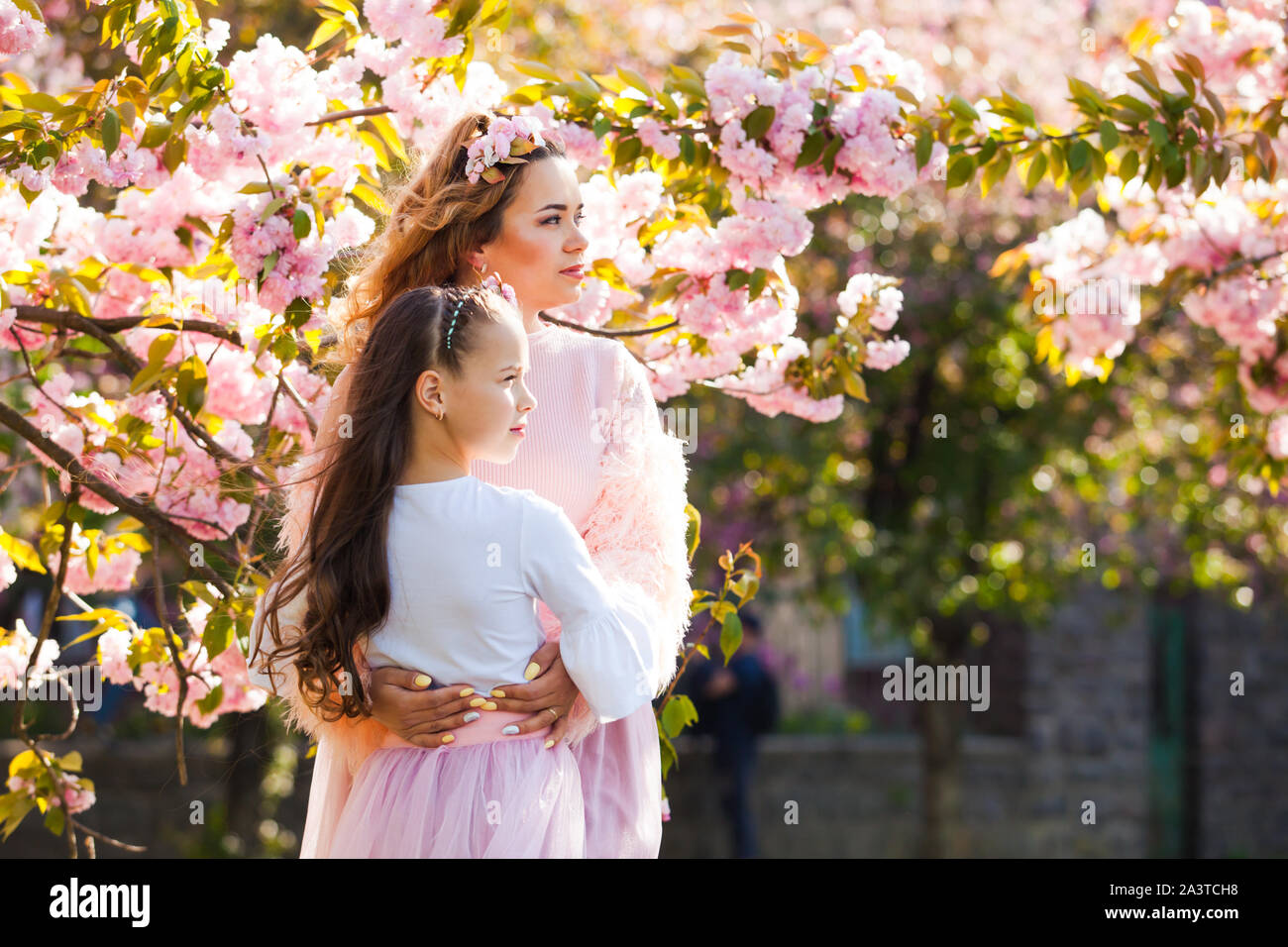 Madre de moda con su hija caminando entre árbol de Sakura. Las mujeres de moda de primavera. Foto de stock