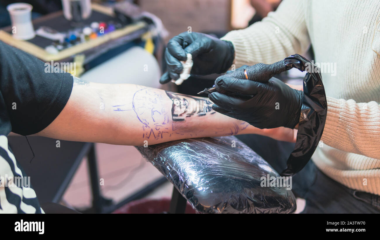Cerca del tatuador profesional haciendo tatuajes en el brazo de un joven  por máquina con tinta negra, tinta negra tatuaje 