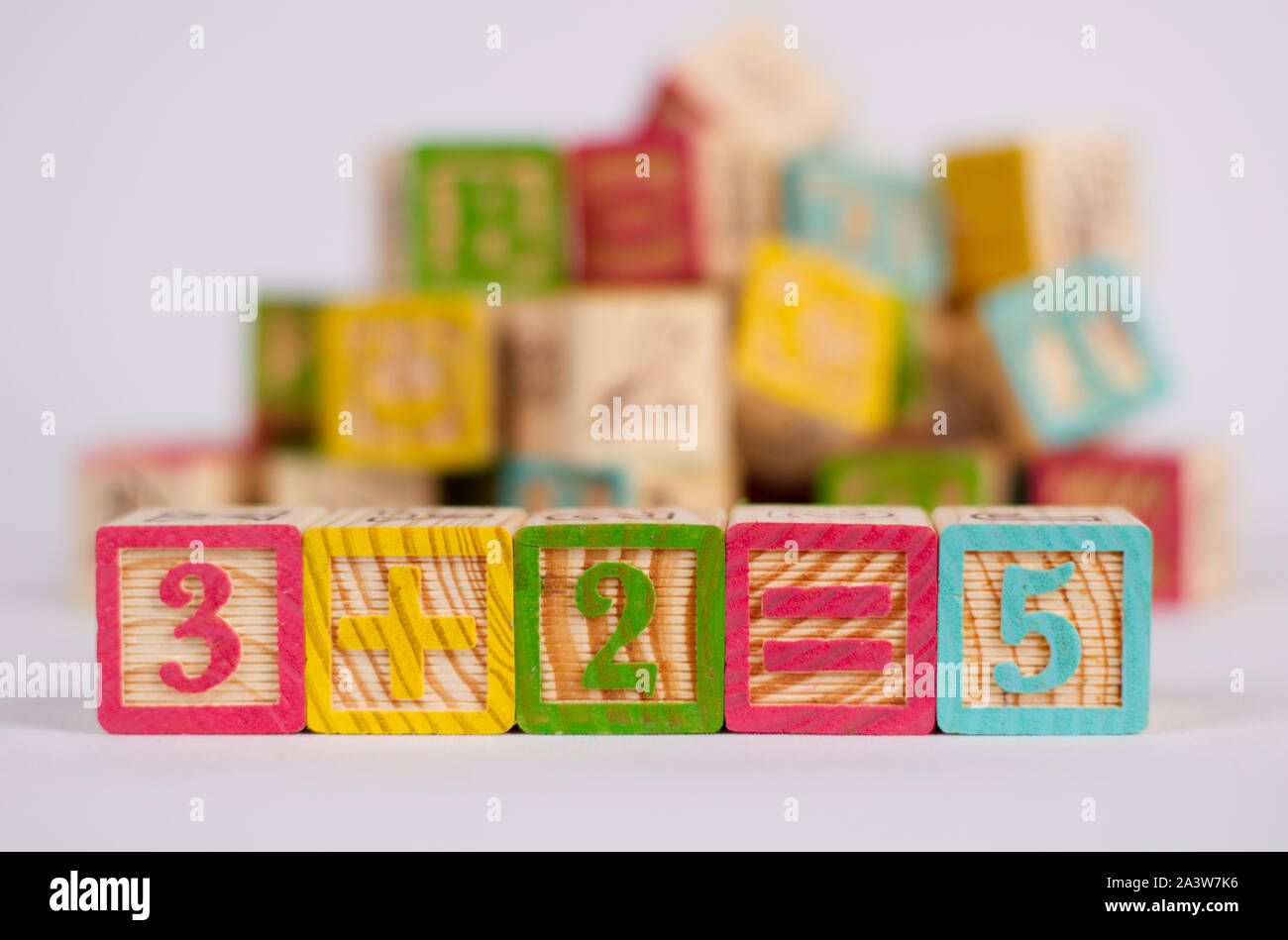 Los números "3+2=5' en bloques de madera de colores, con una luz de fondo. Perfecto para un original y divertido bebé tarjeta o invitación para una babyshower. Foto de stock