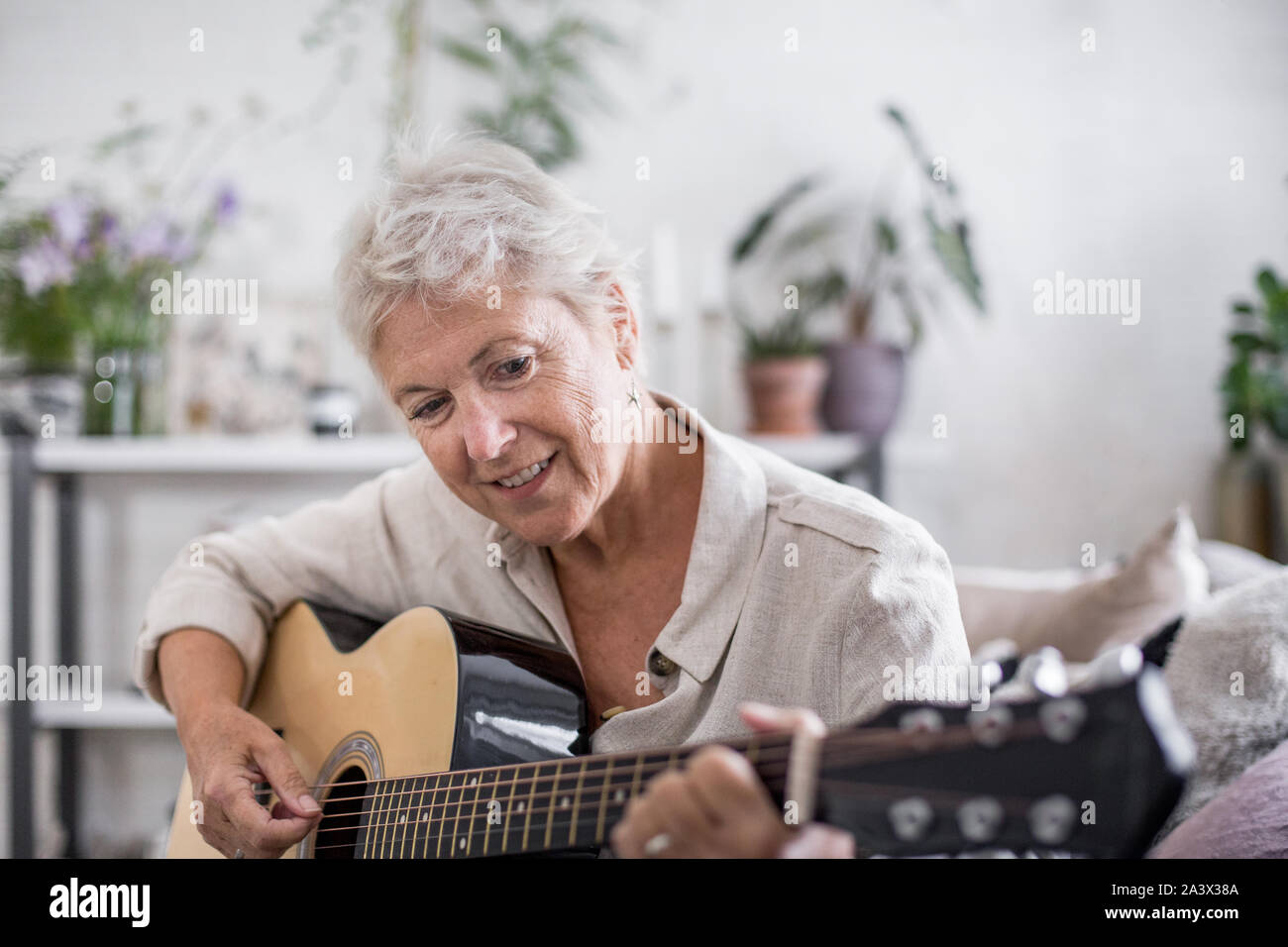 Hembra adulta madura aprendiendo a tocar la guitarra en casa Foto de stock