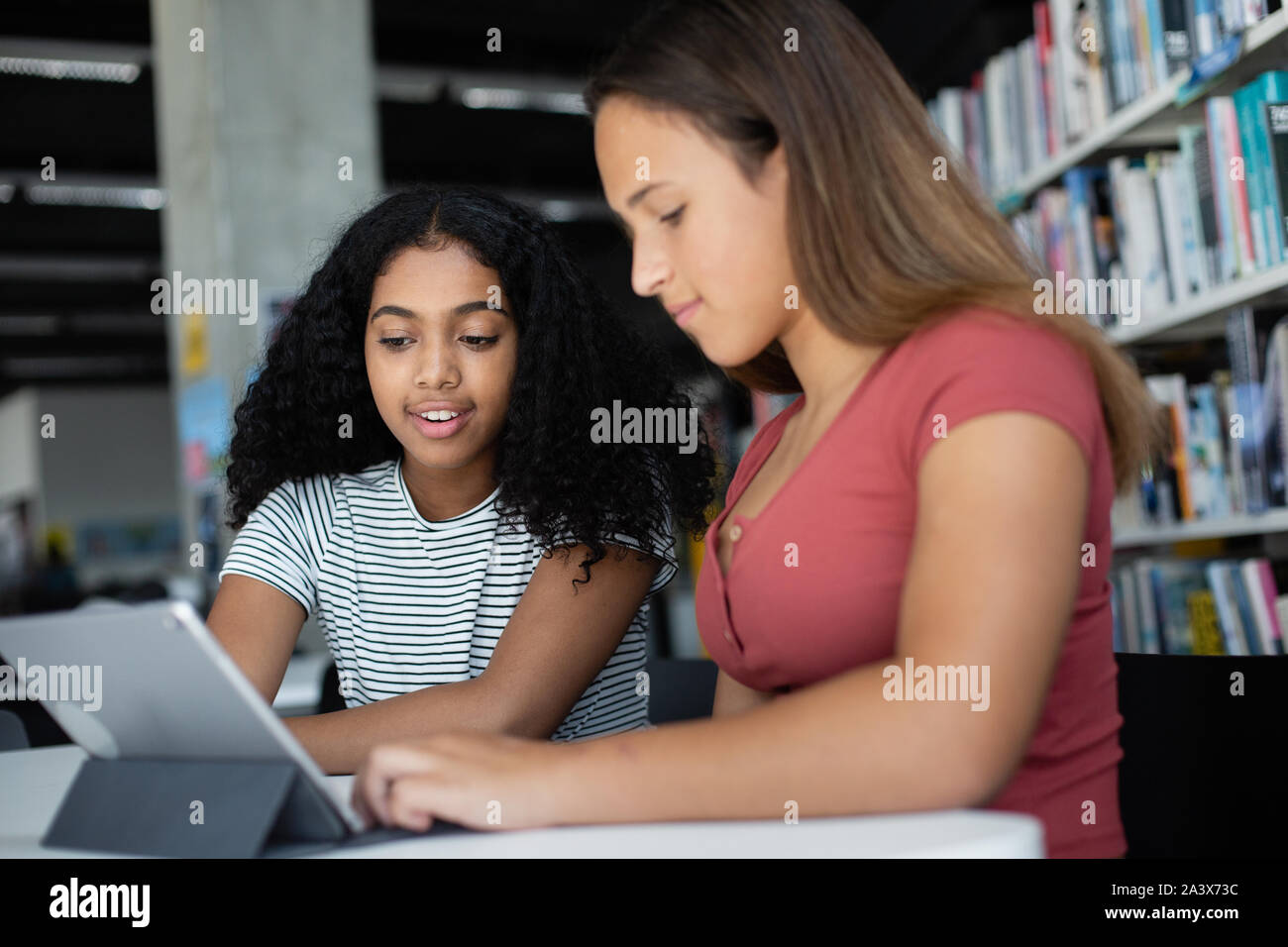 High school alumnas estudiando con tableta digital en la biblioteca Foto de stock