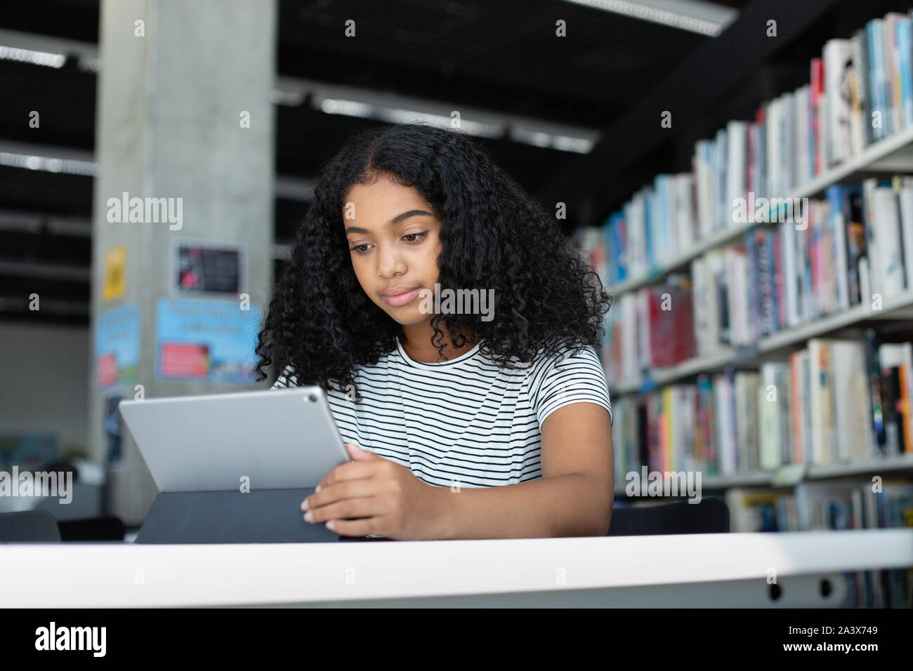 La escuela secundaria femenina afroamericana estudiante con tableta digital en la biblioteca Foto de stock