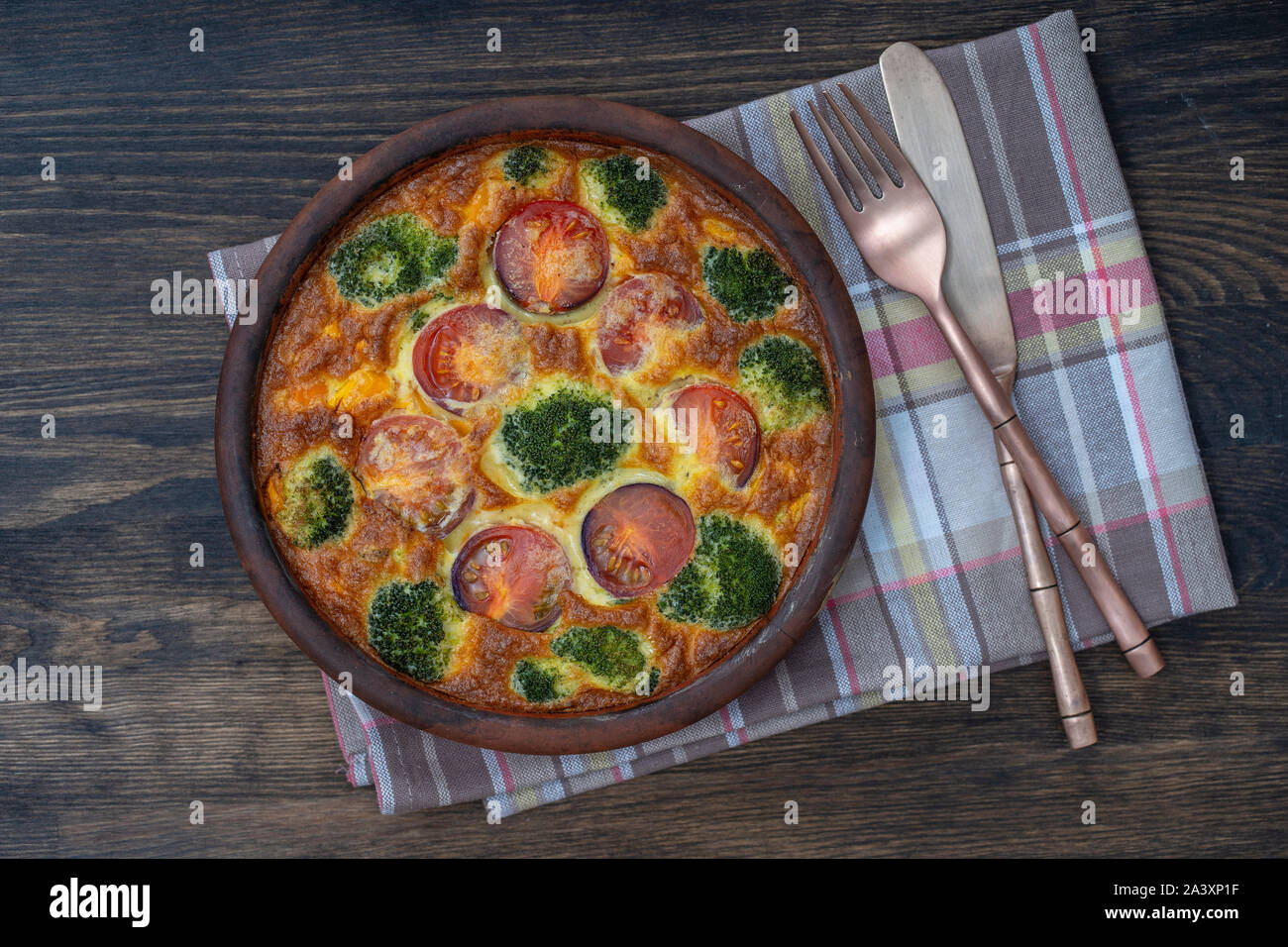 Cuenco de cerámica con verdura frittata, sencilla comida vegetariana. Frittata con huevo, tomate, pimiento, cebolla, brócoli y queso en la mesa de madera, de cerca. Foto de stock