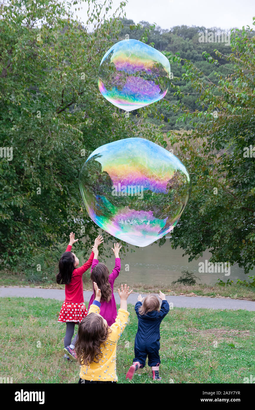 Grupo de niños persiguiendo e intentando atrapar burbujas gigantes. Foto de stock