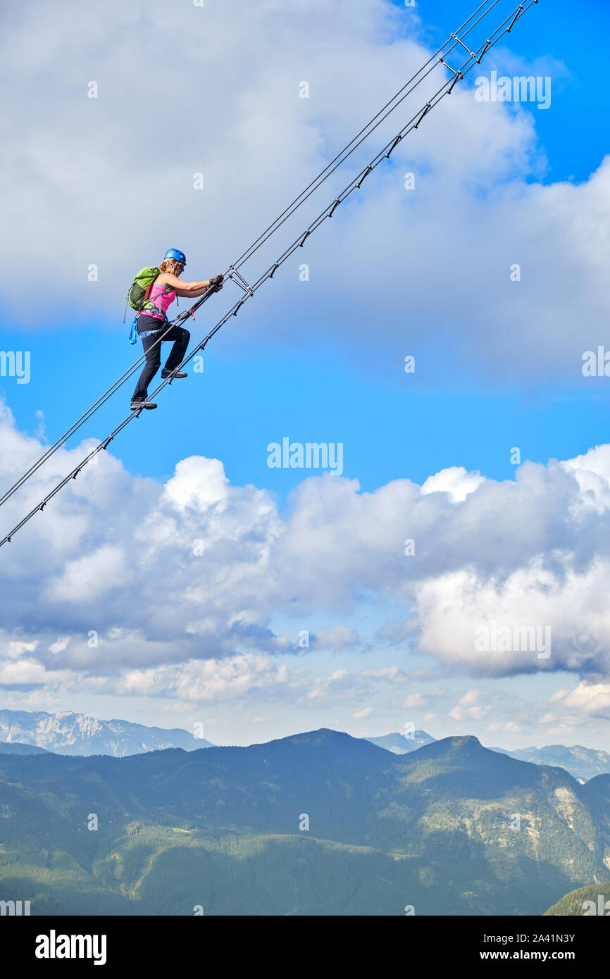 Mujer en la via ferrata Donnerkogel Intersport Klettersteig en los Alpes austriacos, cerca de Gosau. Escalera al cielo concepto. Foto de stock