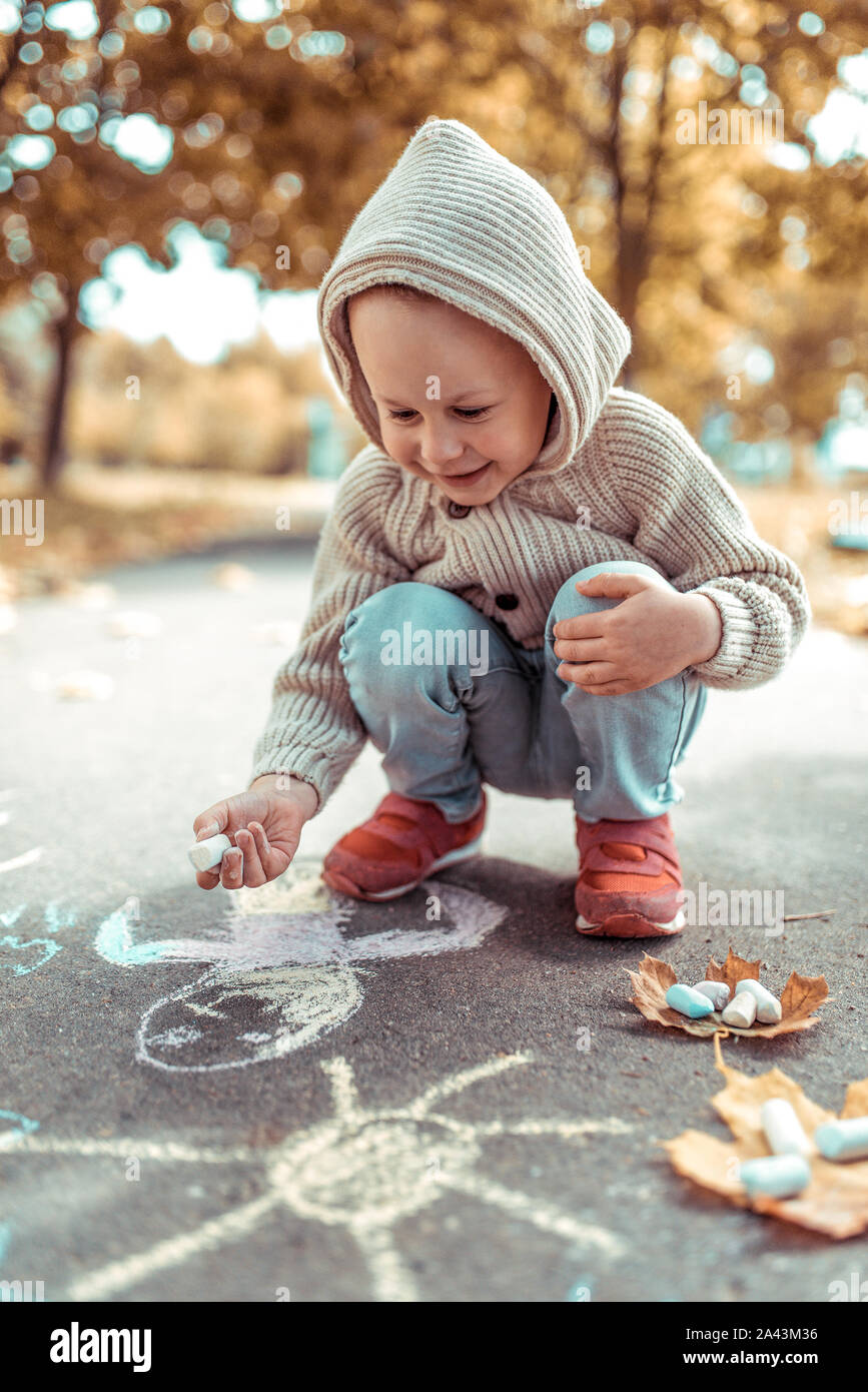 Niño 3-5 años de edad, se dibuja con lápices de colores risas sonrisas regocija, otoño del parque de la ciudad. Ropa abrigadora sudadera con capucha Fotografía de - Alamy