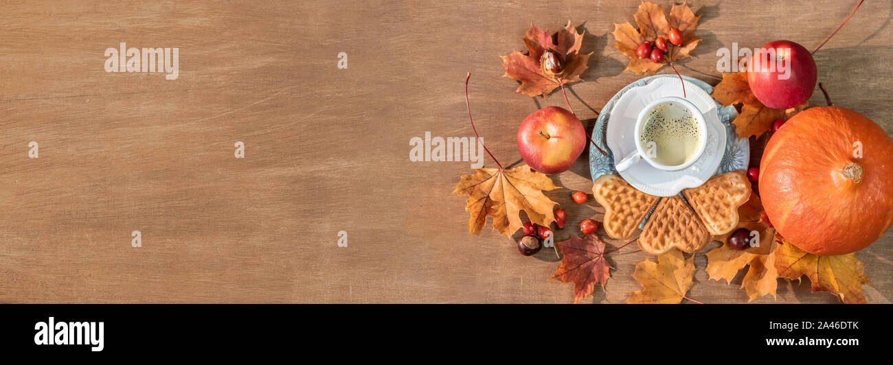 El otoño, caen las hojas, una humeante taza de café caliente, calabaza y un suéter caliente sobre una mesa de madera de fondo. Imagen panorámica Foto de stock