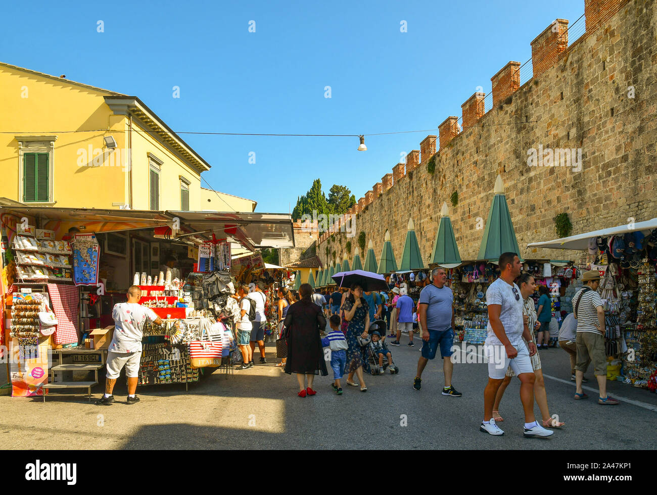 Vista de la calle del famoso destino turístico con gente comprando en puestos de venta de recuerdos y de las antiguas murallas de la ciudad en un día soleado de verano, Pisa, Toscana, Italia Foto de stock