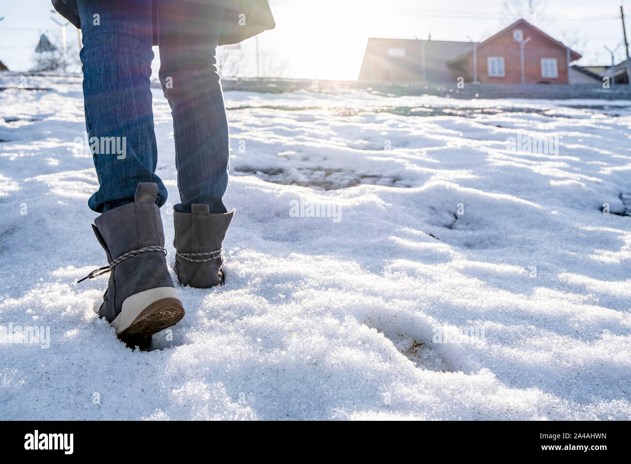 Por separado Cesta Pef Una mujer en gamuza botas sube a una colina cubierta de nieve, los rayos  del sol primaveral, con el telón de fondo de las casas. País camine  Fotografía de stock - Alamy