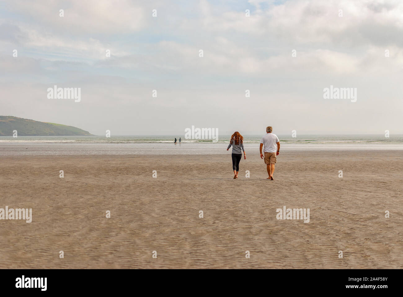 Par de caminar en la playa de arena dejando huellas en la arena. Un padre y su hija disfrutando del día. Día nublado. Foto de stock