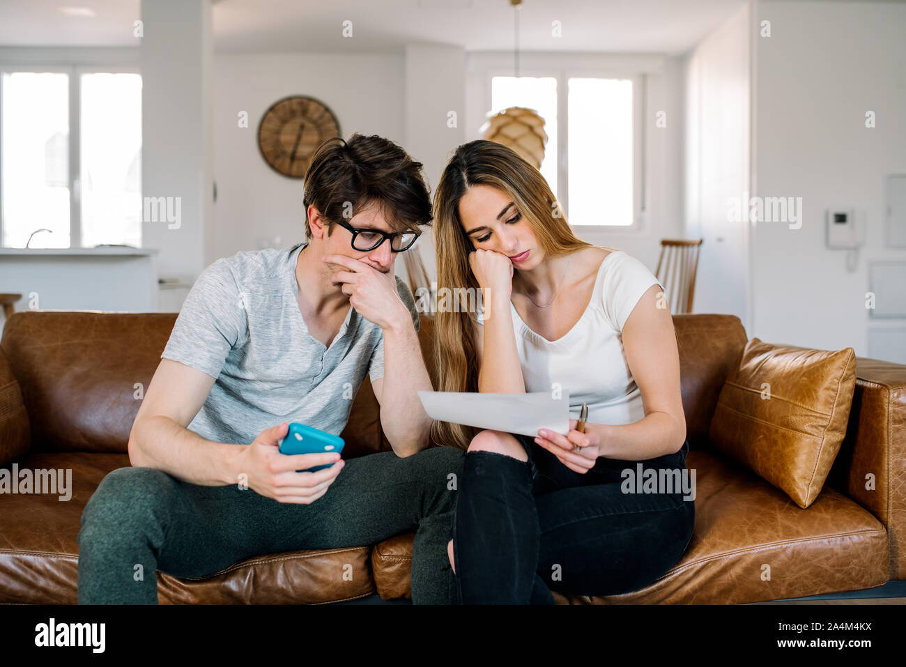 Matrimonio joven con problemas financieros y estrés emocional realizar cálculos con papel trabaje sentado en el sofá en casa Foto de stock
