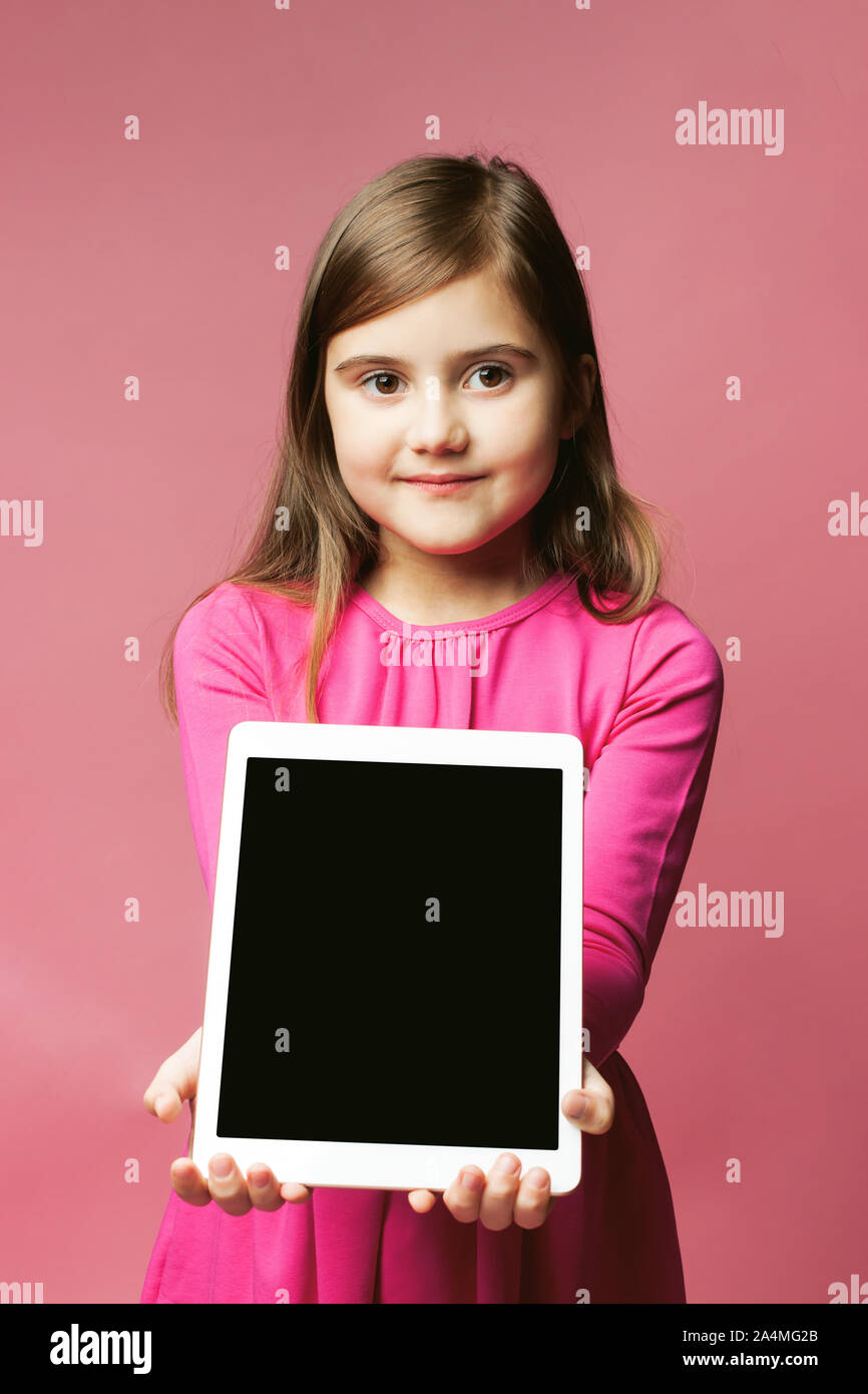 Bonita Chica sujetando una tableta con una pantalla negra. Vestido rosado y  fondo de color rosa. Lugar para el texto. El concepto de ofertas especiales  para niñas, ventas, promociones, etc Fotografía de