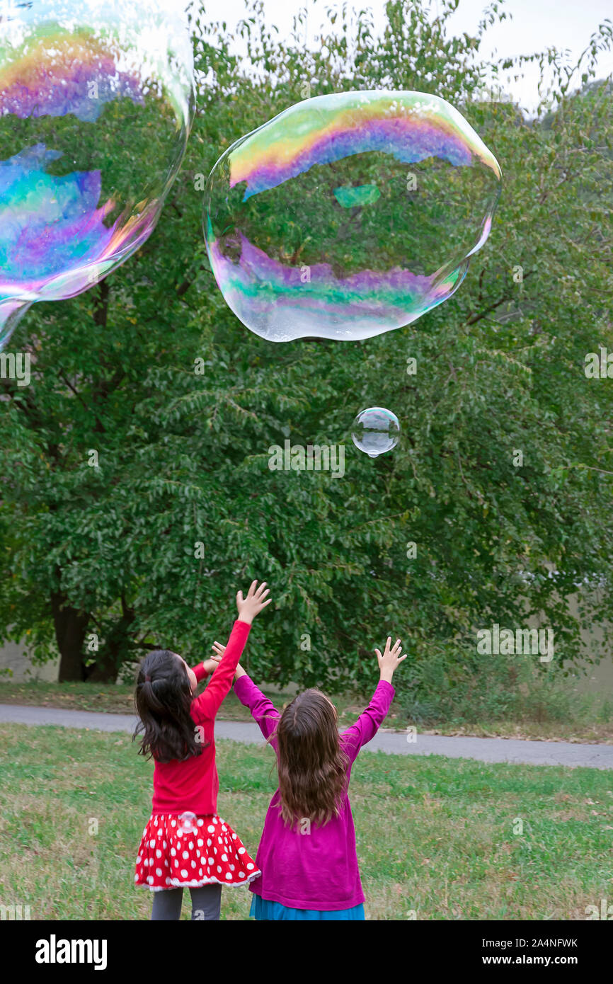 Dos niñas llegando y tratando de atrapar burbujas gigantes. Foto de stock