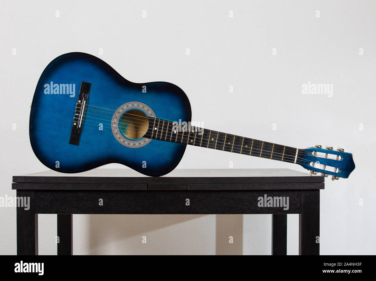 Guitarra acústica azul sobre una tabla de madera negra aislado sobre la pared gris de fondo. Instrumento musical de moda para tocar buena música. Concepto inspirador Foto de stock