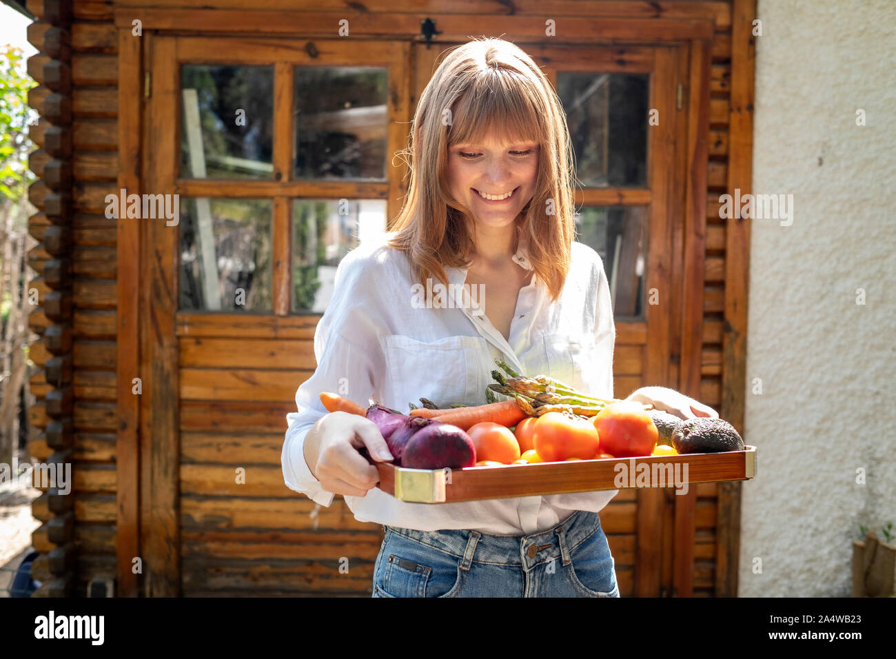 Mujer caucásica sonriendo con una bandeja de madera rellenas con frutas Foto de stock