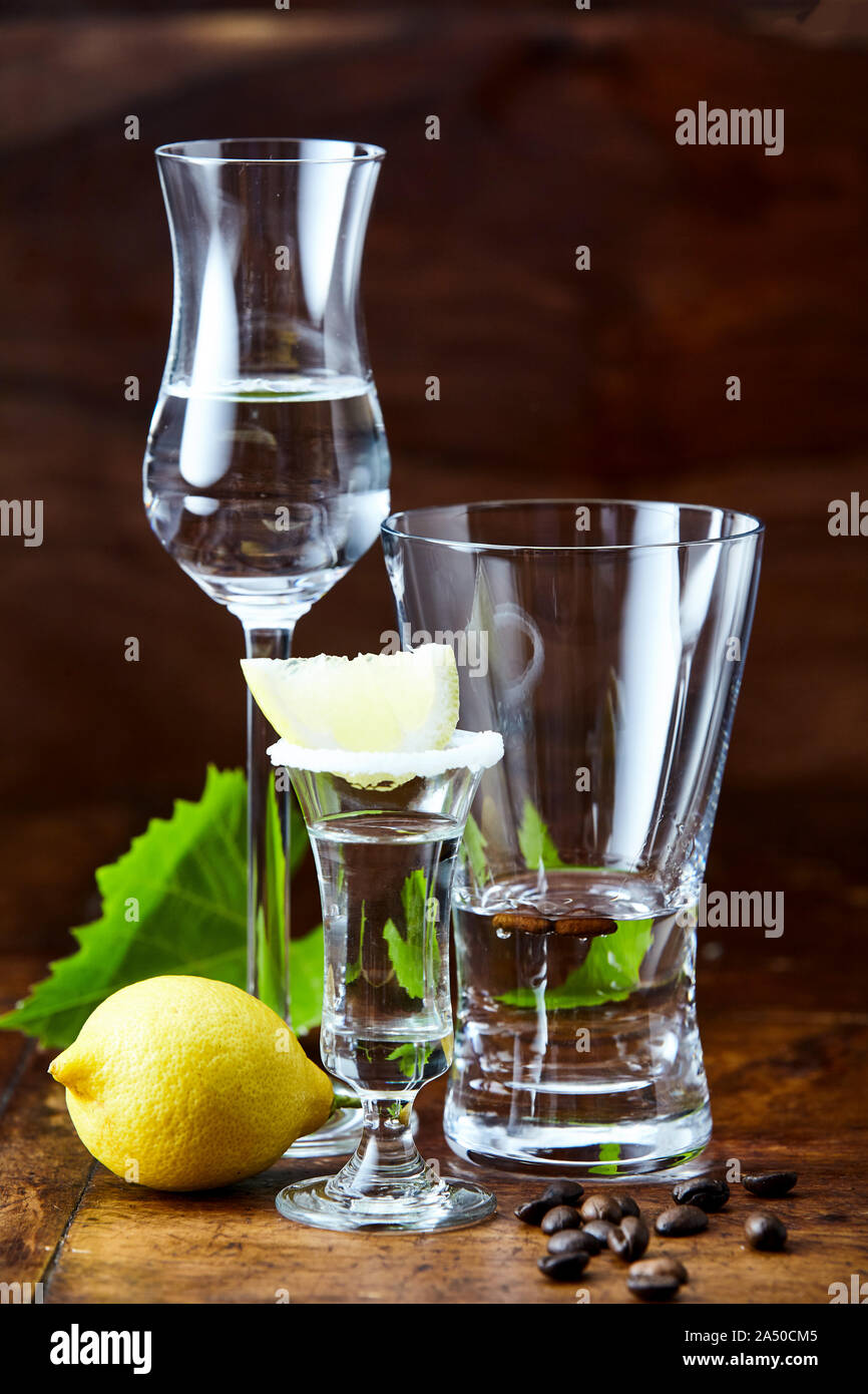 Variedad de vasos para beber grappa transparente con bebidas alcohólicas,  servidas con limón y granos de café. Visto desde el lado de cerca en la  oscuridad Fotografía de stock - Alamy