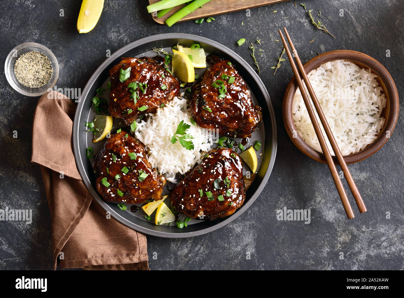Dulce y picante miel muslos de pollo asado con arroz en mesa de piedra oscura. Comida sabrosa en un estilo asiático. Vista superior, laicos plana Foto de stock