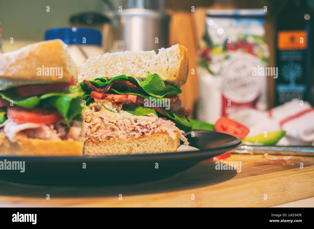 Turquía club sándwich cortado por la mitad con tocino, tomate, aguacate y lechuga en pan de masa fermentada recién horneados. Foto de stock