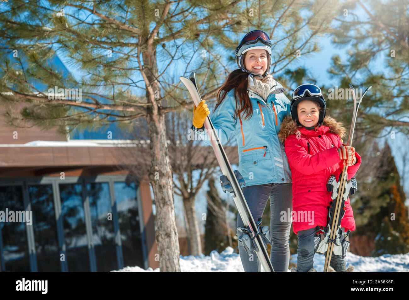 Vacaciones de invierno. La familia juntos al aire libre la mujer y niña en gafas con esquíes posando mostrando thum arriba sonriendo alegre Foto de stock
