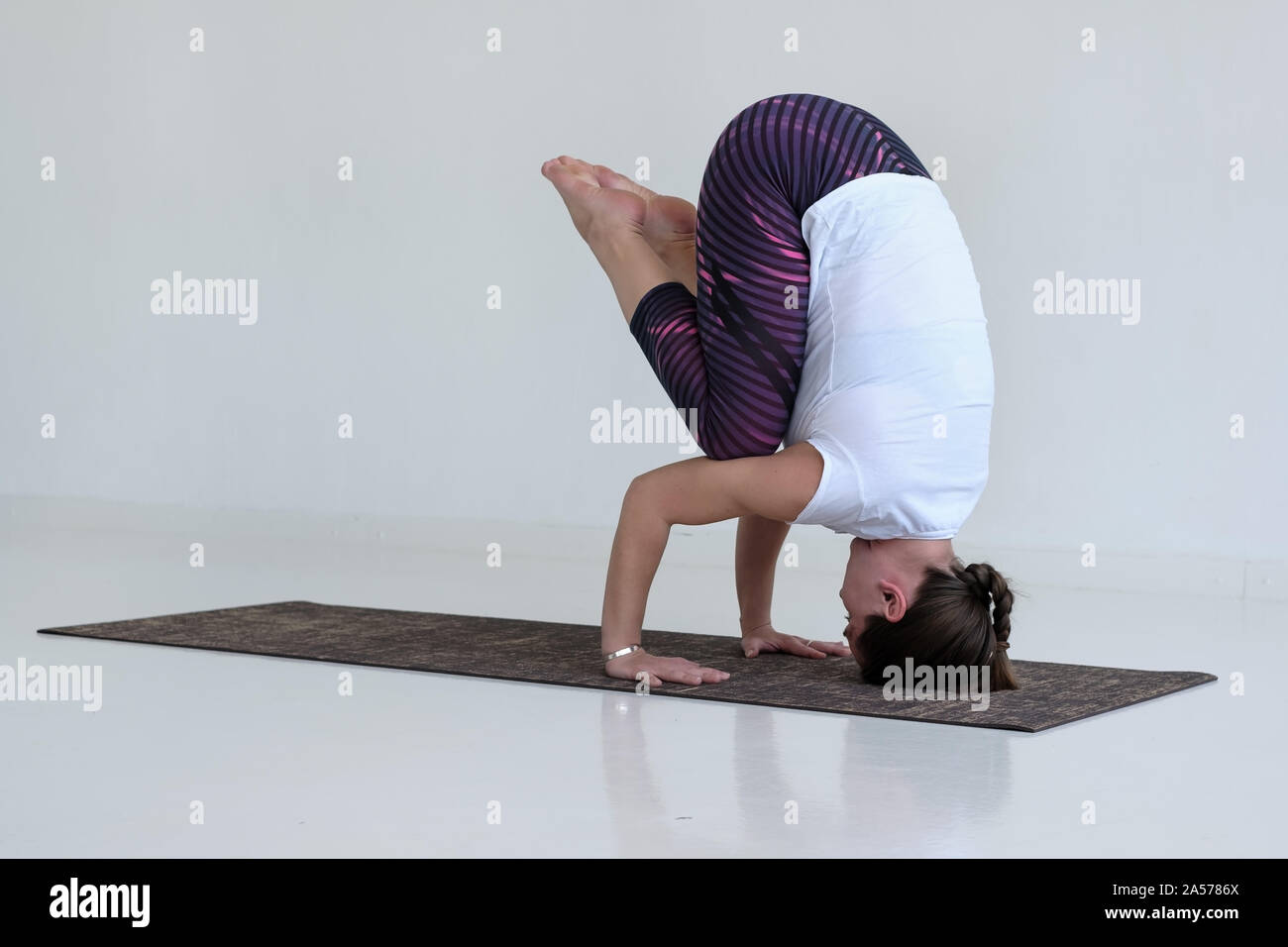 Mujer rubia en un mono deportivo cerrado de color azul practicando yoga se  sienta en un fitball con los brazos levantados en una habitación cerca de  la pared