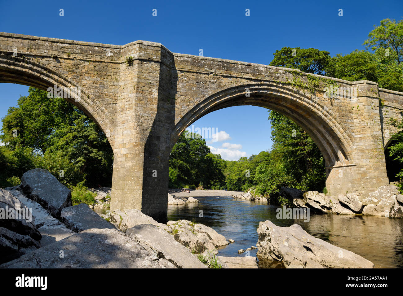 Siglo XIV Puente del Diablo sobre el río Lune en Kirkby Lonsdale con bañistas bajo un cielo azul Cumbria Inglaterra Foto de stock