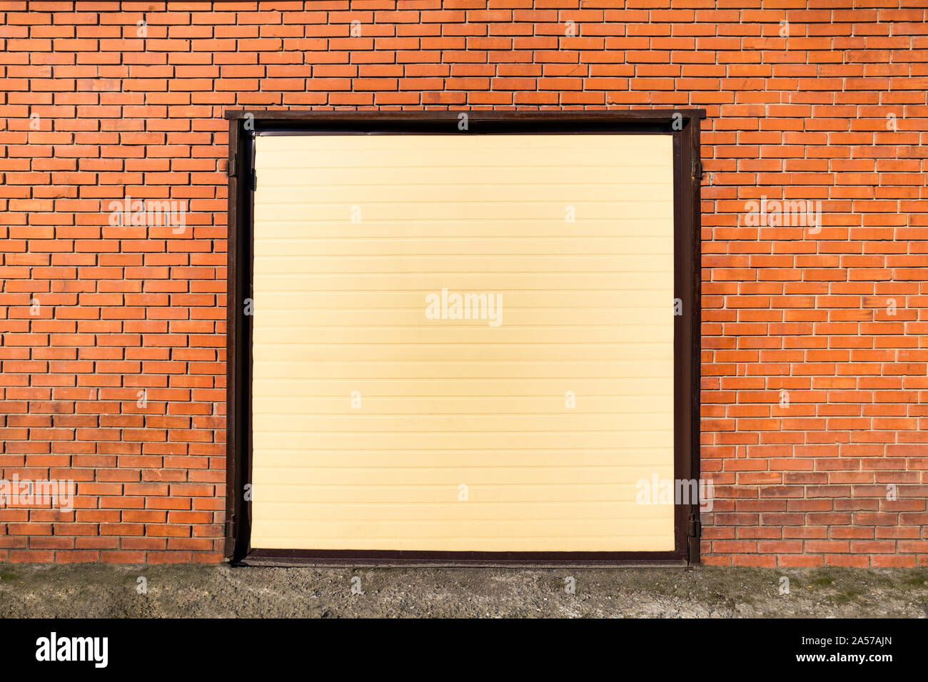 Fachada de un amarillo anaranjado a un garaje con una puerta cerrada en una pared de ladrillo fuera de hierba verde. Puertas automáticas Foto de stock