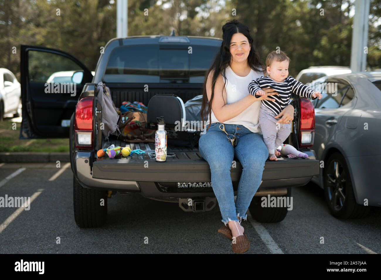 Una joven y su bebé sentarse en Compuerta trasera de un camión en una parada de descanso. Foto de stock