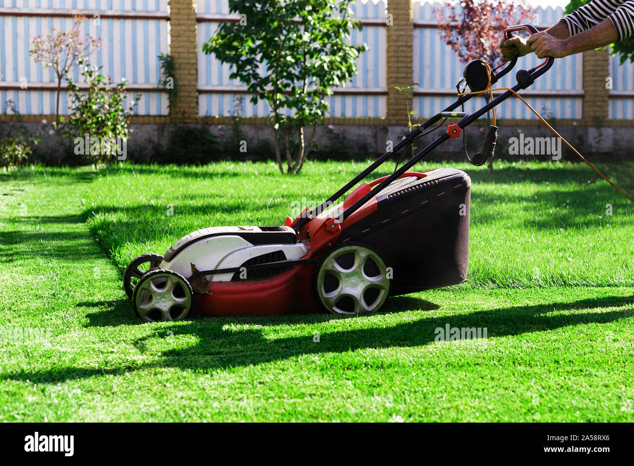 Jardinero por el cortacésped eléctrico cortando el pasto verde en el  jardín. Meadow jardín césped de corte. Chico trabajador de campo de pasto  cortado. Concepto de mantenimiento Care de traspatio Fotografía de