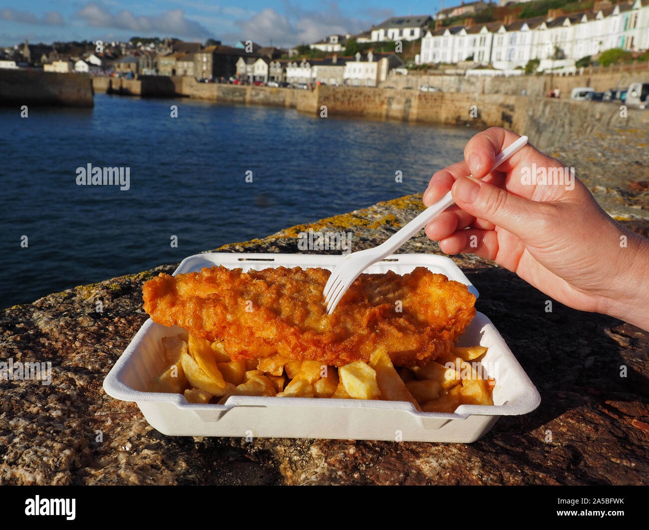 Fish and Chips, pescado y patatas fritas tradicional inglés, cerca de la porción de pescado y patatas fritas en Porthleven Harbour, Cornualles, en el REINO UNIDO Foto de stock