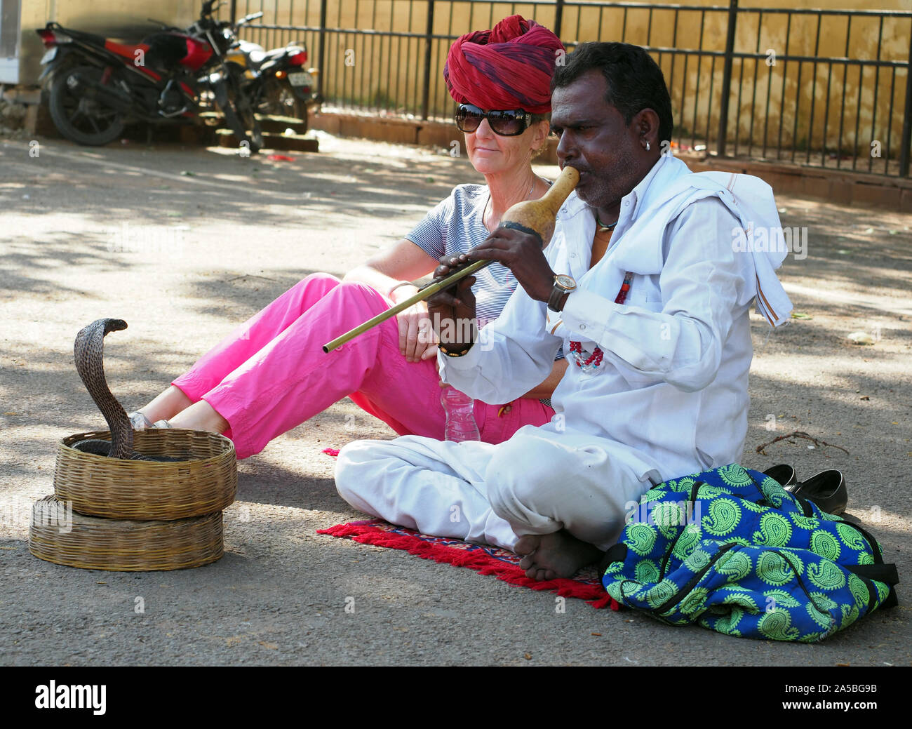 Turista se sienta con un domador de serpientes cobra en Jaipur, Rajasthan, India. Foto de stock