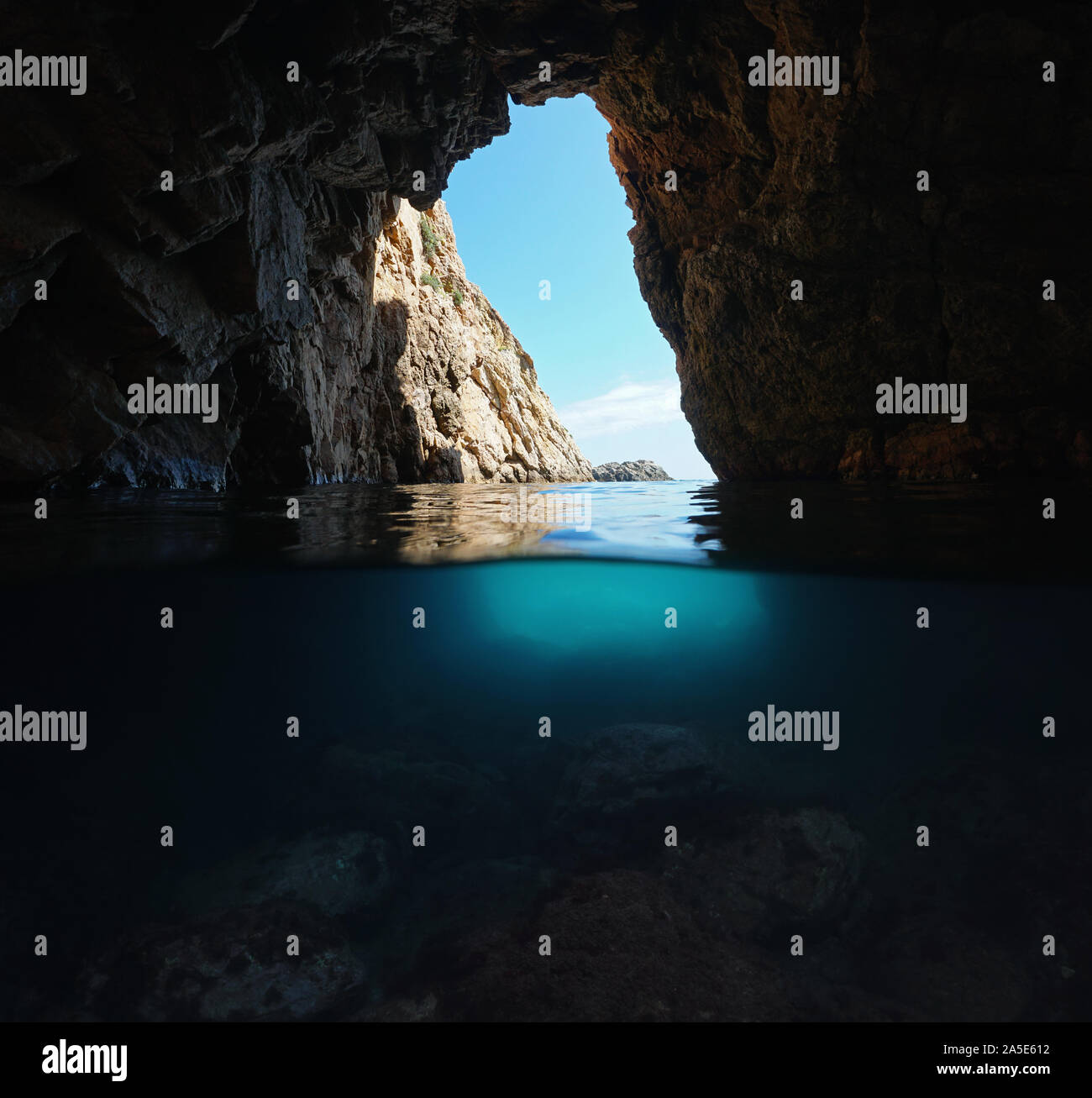 Bajo un arco natural de rocas en la costa del mar Mediterráneo, vista dividida sobre y bajo el agua, España, Costa Brava, Cataluña, Palamos Foto de stock