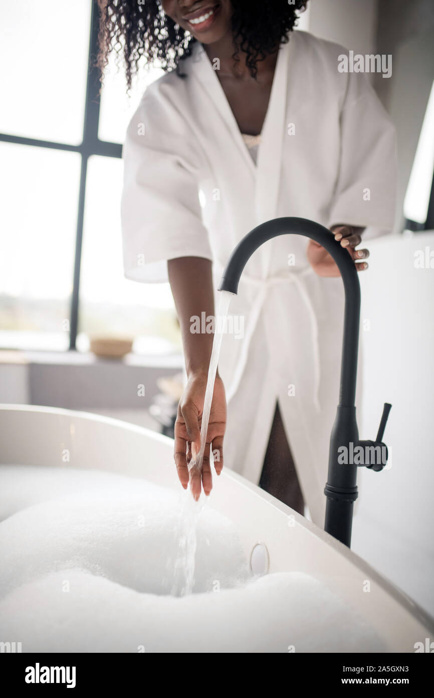 Mujer tratando de temperatura de agua mientras se prepara el baño Foto de stock