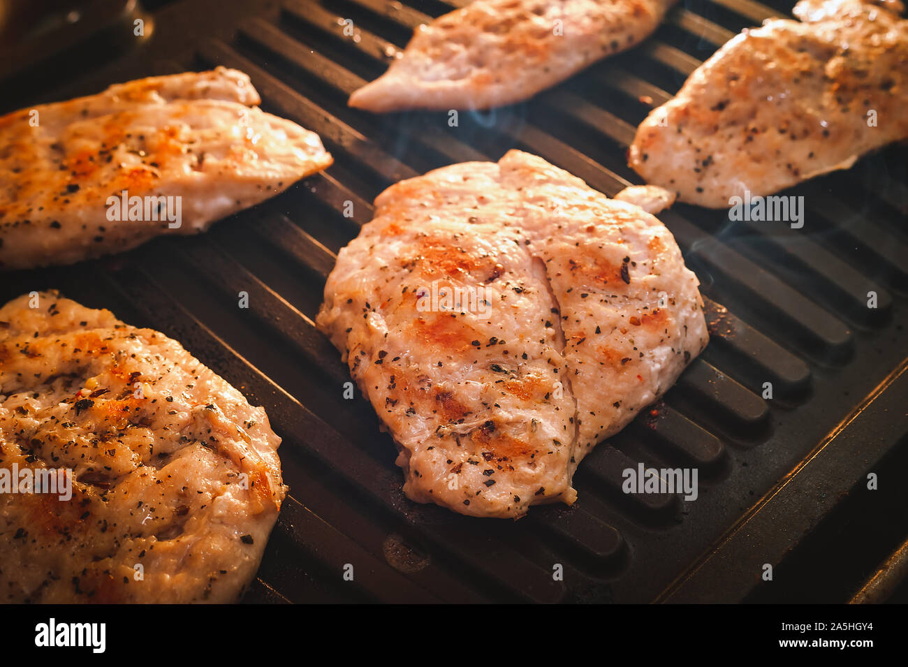 Fumante asar filetes de carne de pollo o pavo condimentado con especias en parrilla eléctrica placa. Foto de stock
