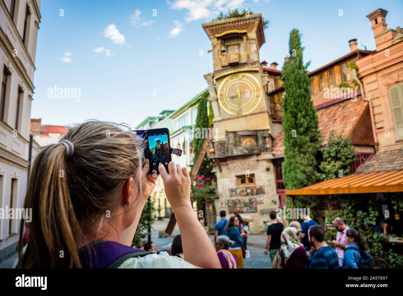 Mujer joven tomando fotos con auto de teléfono reloj inclinada Torre de Tbilisi, Georgia Foto de stock