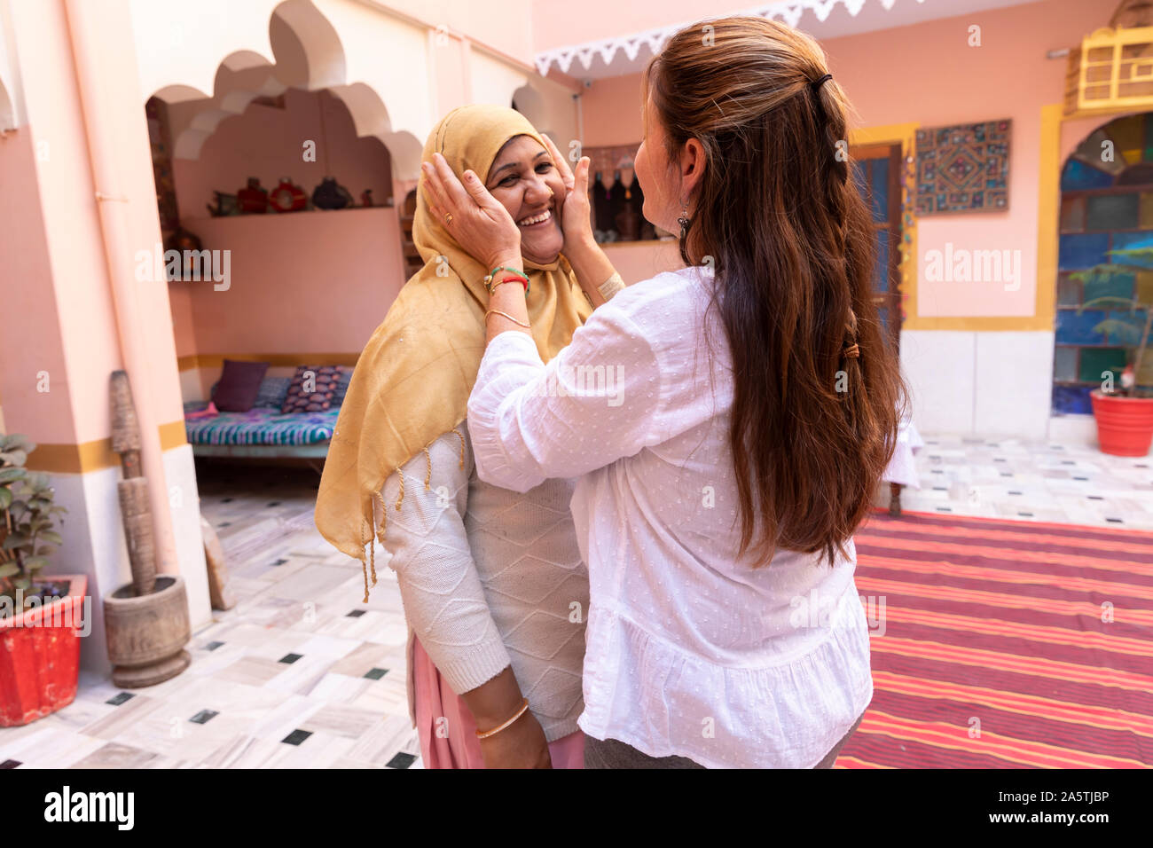Una mujer occidental tazas sus manos alrededor de una mujer india de cara sonriente. Foto de stock