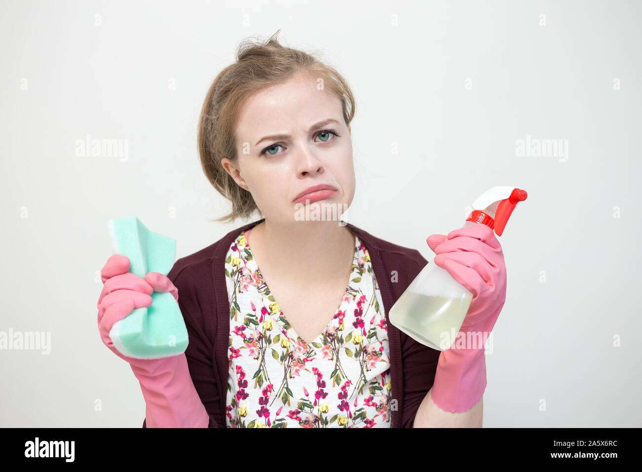 Triste infeliz mujer caucásica joven chica con guantes de goma, la esponja y el pulverizador, limpieza de la casa Foto de stock