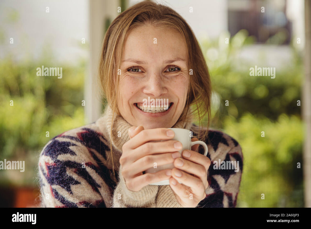 Retrato de mujer sonriente vistiendo un suéter esponjoso sosteniendo una taza Foto de stock